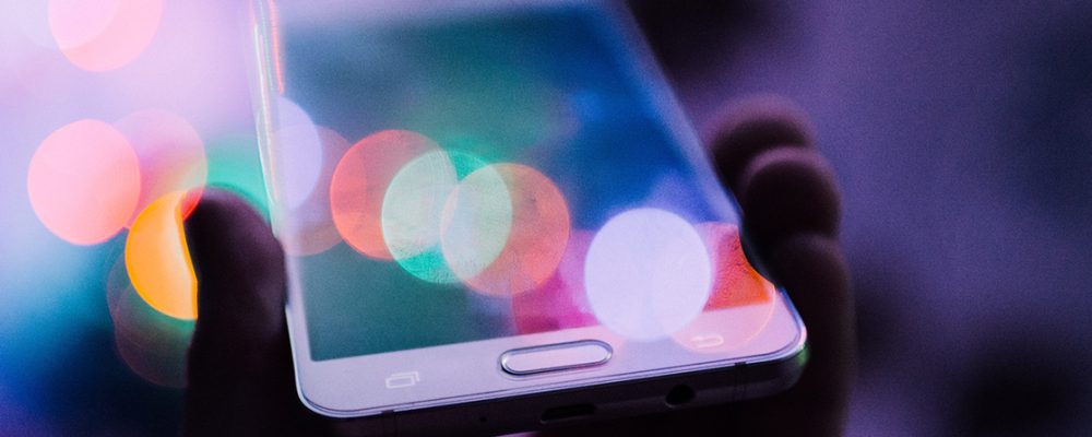 smartphone con bokeh colorato tenuto tra le mani, richiamo ai canali social
